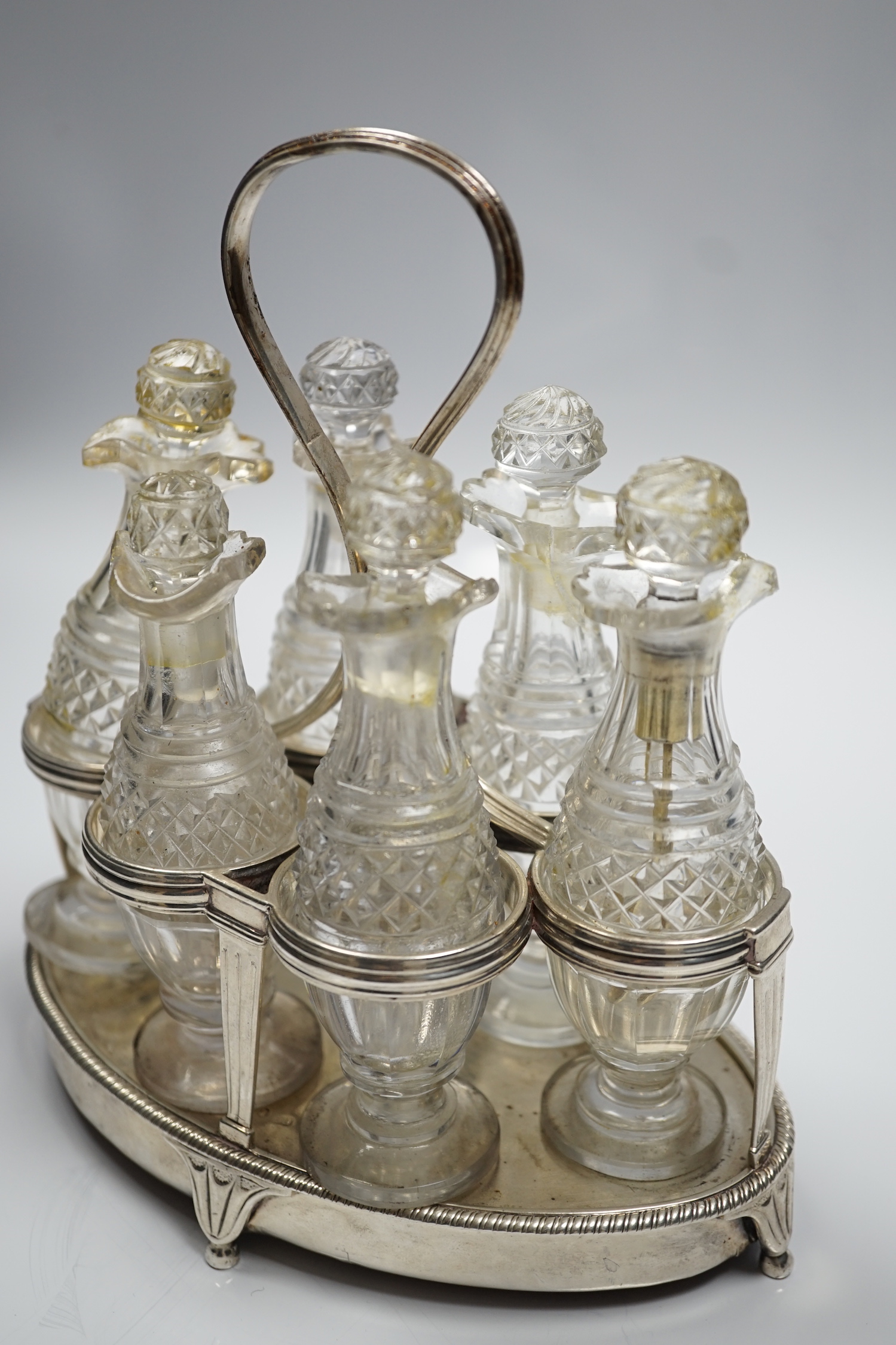 A George III silver mounted oval cruet stand, maker P?, London, 1802, with reeded ring handle and gadrooned border, with six cut glass bottles and stoppers (some damage), height 20cm.